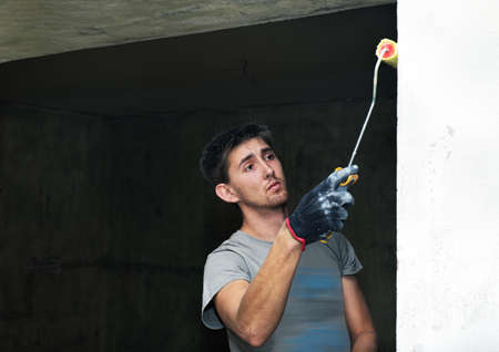 Young man works by painting brush inside of house.