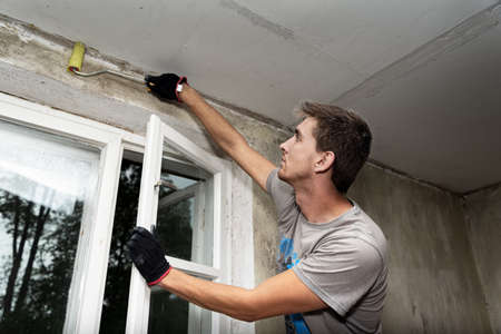 Young man works by painting brush inside of house.