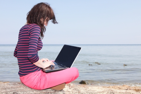 Young woman sitting at the beach with her laptop.の写真素材