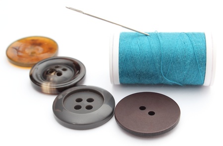 Closeup of sewing buttons and spool of thread with needle. Isolated on white background