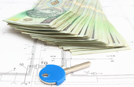 Stack of money with key lying on construction drawing of houseの写真素材