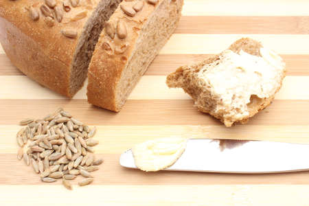 Rye grain, butter on knife and bitten slice of bread lying on wooden cutting boardの写真素材