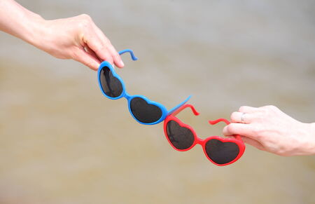 Hands with red and blue sunglasses shaped heart on sea backgroundの写真素材