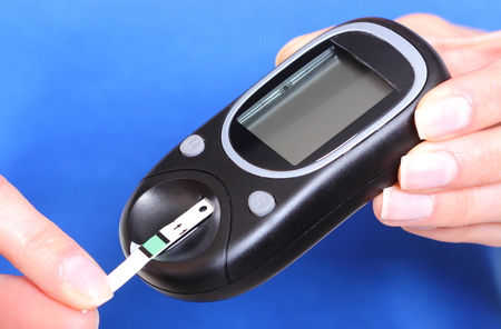 Closeup of strip for glucose testing and glucose meter, measuring sugar level  Isolated on blue backgroundの写真素材