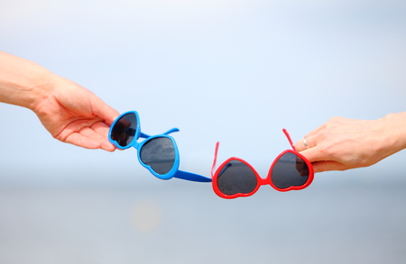 Hands with red and blue sunglasses shaped heart on sky backgroundの写真素材