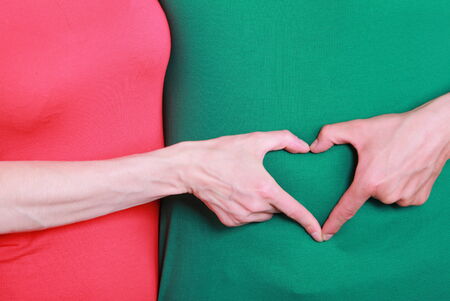 Hand of woman and man arranged in shape of heart on green shirt background, positive emotions
