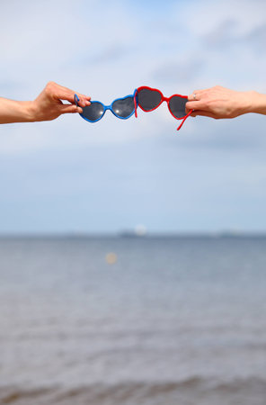 Hands with red and blue sunglasses shaped heart on sky backgroundの写真素材