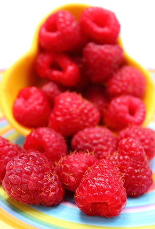 Closeup of fresh raspberries pouring out of yellow bowl on colorful plate