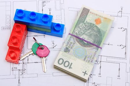 Heap of banknotes, home keys and wall of plastic colorful building blocks lying on construction drawing of house, concept of building houseの写真素材