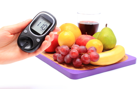 Hand of woman with glucose meter and fresh natural fruits on cutting board in background, concept for healthy eating and diabetesの写真素材