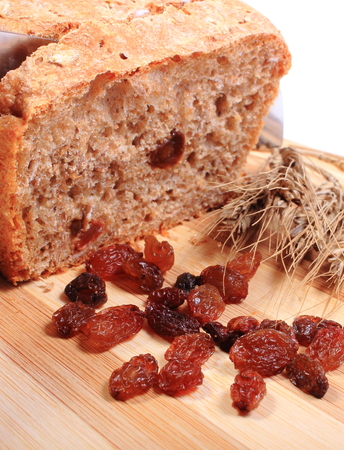 Slicing fresh baked wholemeal bread, ears of wheat and heap of raisins lying on cutting board, concept for healthy eatingの写真素材