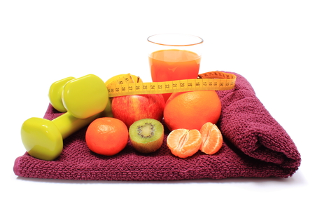 Fresh fruits with tape measure, glass of juice and green dumbbells for fitness lying on purple towel, concept for slimming, healthy nutrition and strengthening immunityの写真素材