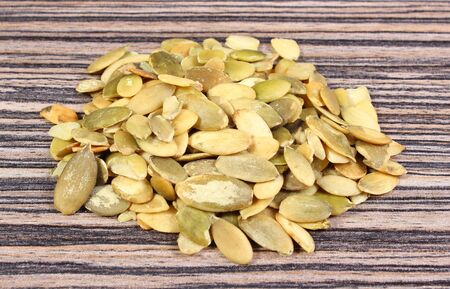 Heap of pupkin seeds lying on wooden background, concept for healthy nutrition