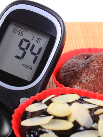 Glucose meter and homemade delicious fresh baked chocolate muffins in red silicone cups, concept for diabetes and dessertの写真素材