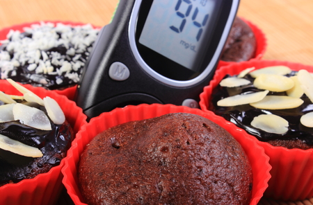 Glucose meter and homemade delicious fresh baked chocolate muffins in red silicone cups, concept for diabetes and dessertの写真素材