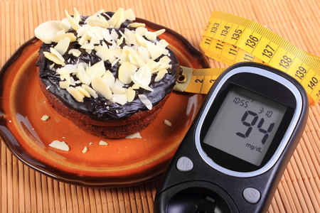 Glucose meter, homemade delicious fresh baked chocolate muffins with sliced almonds on brown plate and tape measure, concept for diabetes, slimming and dessertの写真素材
