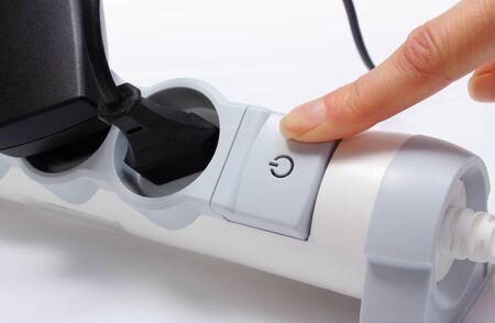 Finger of woman turns off electrical extension, electrical plugs with cords connected to electrical...
