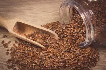 Vintage photo of brown linseed, flax seeds spilling out of glass jar on wooden background, concept for healthy nutritionの写真素材