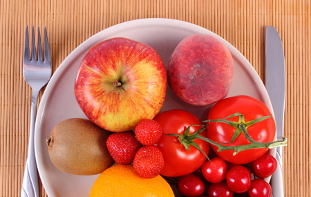 Fresh ripe fruits and vegetables lying on plate and cutlery on wooden surface, concept of healthy food, nutrition and strengthening immunity