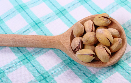 Roasted pistachio nuts with wooden spoon on checkered tablecloth, healthy food and nutritionの写真素材