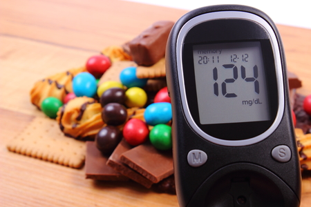 Glucose meter with heap of candies and cookies on wooden table, too many sweets, concept of diabetes and reduction of eating sweetsの写真素材