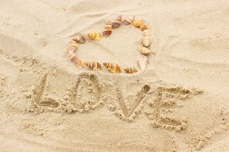 Word love written on sand at the beach and heart of shells, symbol of love, summer timeの写真素材