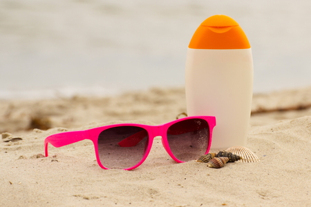 Shells, pink sunglasses and sun lotion on sand at the beach, seasonal concept, protection from sun