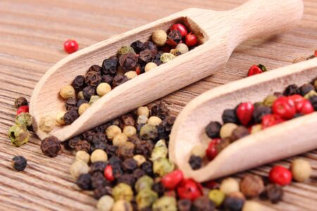 Heap of fresh colored pepper with wooden spoon lying on wooden tableの写真素材