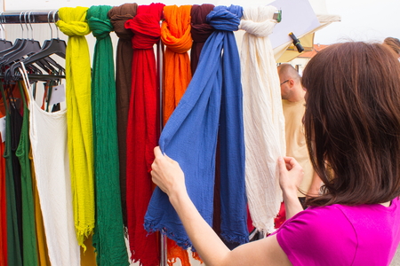 Woman looking at clothing hanging on hangers, shopping clothes on stall at the bazaarの写真素材