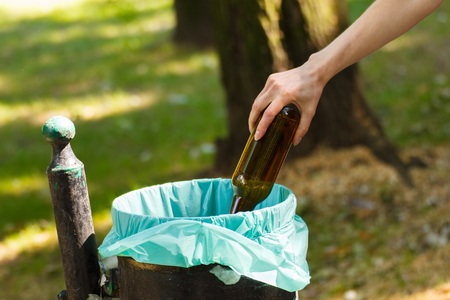 Hand of woman throwing glass bottle into old trash can, concept of environmental protection, littering of environmentalの写真素材