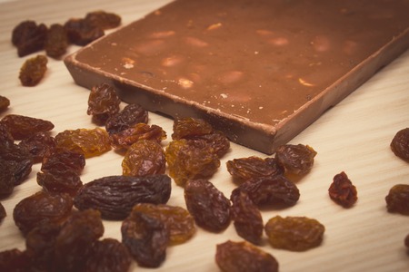 Vintage photo, Nutritious chocolate with hazelnuts and heap of raisins on wooden tableの写真素材