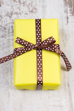 Wrapped in yellow paper gift for Christmas, birthday or other celebration on old wooden white plankの写真素材