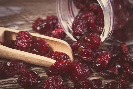 Vintage photo, Heap of red cranberries with spoon spilling out of glass jar on wooden table, concept...