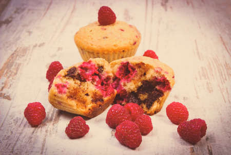 Vintage photo, Homemade fresh baked muffins with chocolate and raspberries on old rustic wooden background, delicious dessertの写真素材