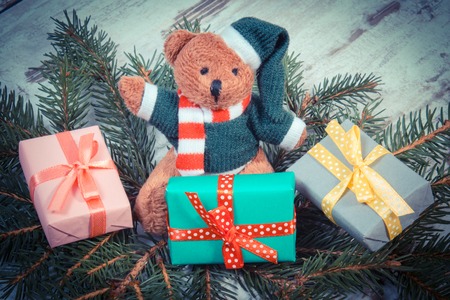 Vintage photo, Fluffy teddy bear with wrapped colorful gifts for Christmas or other celebration and green spruce branches on old wooden white tableの写真素材