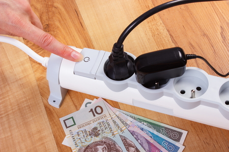 Finger of woman turns off electrical power strip with connected plug, polish currency money, concept...
