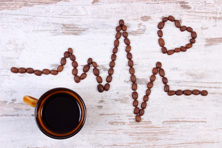 Electrocardiogram line of roasted coffee grains and cup of hot coffee on rustic wooden background, ecg heart rhythm, medicine and healthcare conceptの写真素材