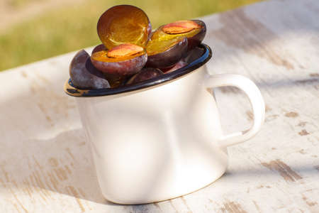 Heap of fresh plums in metallic mug lying on wooden rustic table in garden on sunny day, healthy nutritionの写真素材