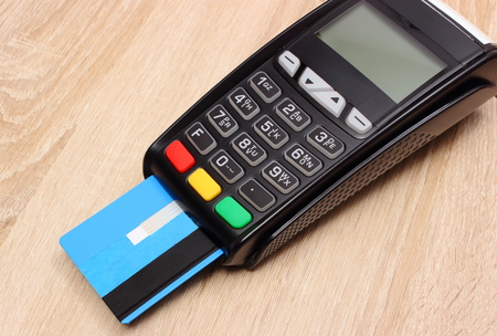 Payment terminal with credit card on wooden desk, credit card reader, paying using credit card,...