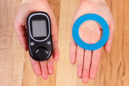 Glucose meter and blue circle of paper in hand, symbol of diabetic and fight against diabetes
