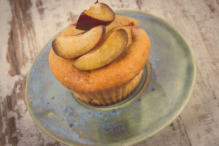 Vintage photo, Homemade fresh baked muffins with plums on plate on old rustic wooden background, delicious dessertの写真素材