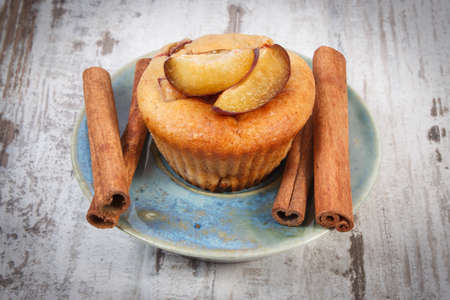 Homemade fresh baked muffins with plums and cinnamon sticks on plate on old rustic wooden background, delicious dessertの写真素材