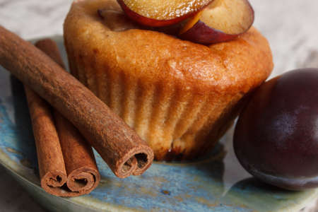Homemade fresh baked muffins with plums and cinnamon sticks on plate on old rustic wooden background, delicious dessertの写真素材