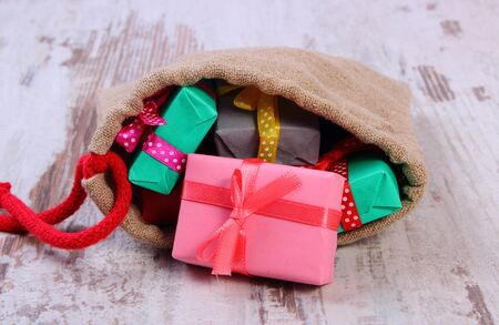 Wrapped colorful gifts for Christmas, birthday or other celebration in jute bag lying on old wooden white tableの写真素材