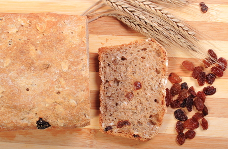 Slice of fresh baked wholemeal bread, ears of wheat and heap of raisins lying on cutting board, concept for healthy eatingの写真素材