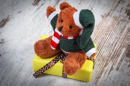 Fluffy teddy bear with wrapped yellow gift for Christmas, birthday, valentines or other celebration on old wooden white tableの写真素材