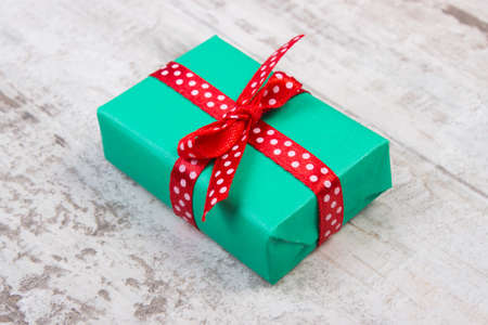 Wrapped in green paper gift for Christmas, birthday or other celebration on old wooden white plankの写真素材