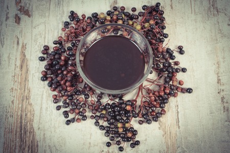 Vintage photo, Bunch of fresh elderberry and glass of elderberry juice on old rustic wooden background, healthy nutrition, alternative medicine and therapyの写真素材