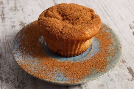 Homemade fresh baked muffins with powdery cinnamon on plate on old rustic wooden background,...