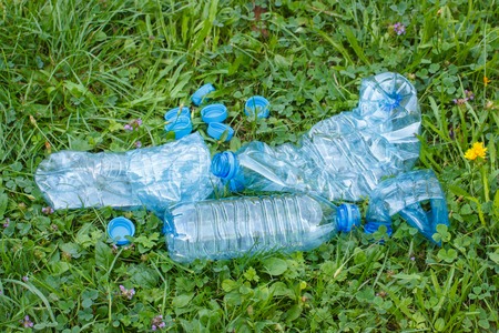 Crushed plastic bottles of mineral water and bottle caps on grass in park, concept of environmental protection, littering of environmentの写真素材
